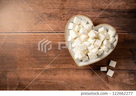White sugar cubes in a heart shaped bowl on wooden background. Top view, copy space 122662277