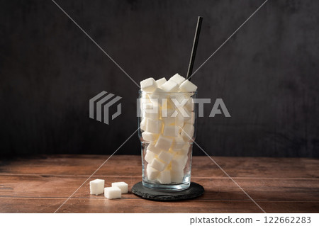Sugar addiction. Glass full of white sugar cubes - unhealthy diet concept. Sugar addiction. Glass full of white sugar cubes - unhealthy diet concept. 122662283