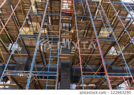 Workers utilize scaffolding to enhance safety and access during the construction of a multi-story building in a busy area Workers utilize scaffolding to enhance safety and access during the construction of a multi-story building in a busy area 122663290