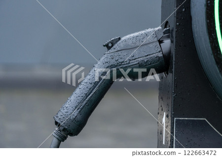 Raindrops glisten on an electric vehicle charging handle, highlighting a commitment to sustainable energy and modern transportation in cities 122663472