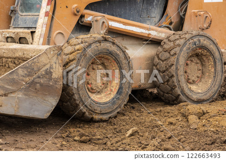 A backhoe and bulldozer are busy digging and maneuvering through dirt at an active construction site as workers coordinate their efforts nearby A backhoe and bulldozer are busy digging and maneuvering through dirt at an active construction site as workers coordinate their efforts nearby 122663493