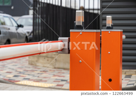 An automatic barrier gate stands closed, controlling entry to a well-organized parking lot, ensuring safety and security for vehicles An automatic barrier gate stands closed, controlling entry to a well-organized parking lot, ensuring safety and security for vehicles 122663499