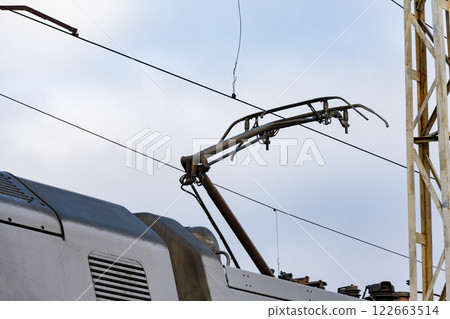 An electric train prepares for departure with its overhead conductor and support system visible against a clear daytime sky 122663514