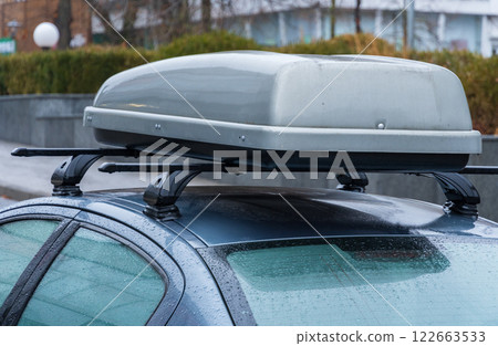 A sleek car is parked in an urban area amidst rain, showcasing its roof-mounted storage accessory, perfect for travel and adventure A sleek car is parked in an urban area amidst rain, showcasing its roof-mounted storage accessory, perfect for travel and adventure 122663533