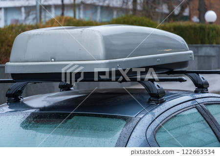 A sleek vehicle is parked on a rainy evening in an urban environment, featuring a rooftop storage box designed for travel and adventure 122663534