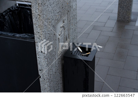 A dark trash bin stands beside a recycling container, emphasizing effective waste management and environmental conservation in the city 122663547
