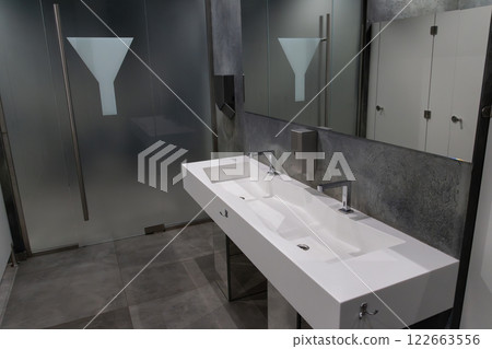 Spacious restroom showcases sleek frosted glass and a stylish dual sink with minimalist faucets, emphasizing hygiene and modern design 122663556