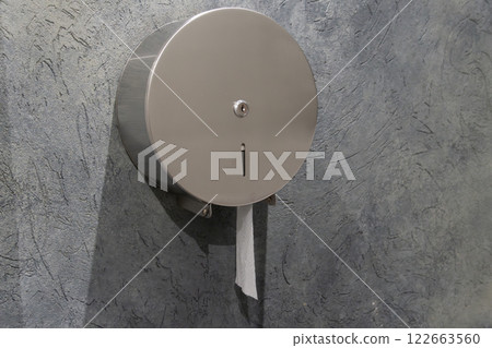 A round stainless steel toilet paper dispenser is installed in a gray wall, promoting hygiene and cleanliness in the restroom area 122663560