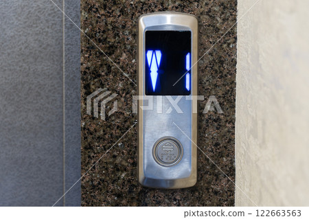 Control panel displays illuminated buttons indicating elevator direction and floor selection in a contemporary apartment environment 122663563