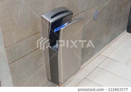 This modern automatic hand dryer is installed in a clean bathroom, providing efficient drying for improved hygiene after handwashing 122663577