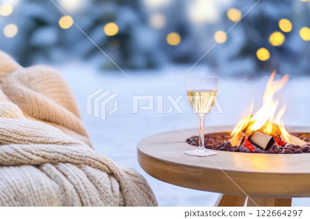 Cozy outdoor seating area featuring a fire pit and wine glass in a winter wonderland setting 122664297
