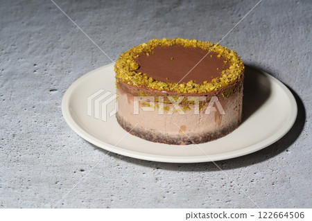 Dubai chocolate cheesecake with pistachio paste and kataifi filling covered in chocolate ganache on white plate. Grey background with copy space. Indulgence, gourmet desserts, art of culinary 122664506