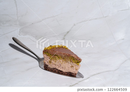 Slice of Dubai chocolate cheesecake with pistachio paste and kataifi covered in chocolate ganache on cake spatula. Marble background with copy space. Indulgence, gourmet desserts, culinary Slice of Dubai chocolate cheesecake with pistachio paste and kataifi covered in chocolate ganache on cake spatula. Marble background with copy space. Indulgence, gourmet desserts, culinary 122664509