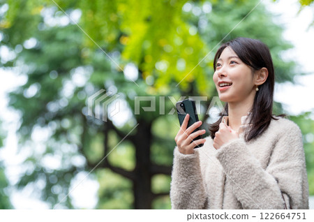A smiling Japanese woman holding a smartphone in the park 122664751