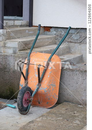 orange wheelbarrow with two handles and one wheel, construction, repair, construction site, house construction, foundation, concrete, DIY construction, metal containers, garbage transportation orange wheelbarrow with two handles and one wheel, construction, repair, construction site, house construction, foundation, concrete, DIY construction, metal containers, garbage transportation 122664808