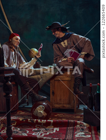 Men, pirates playing card game on dark background with retro globe and nautical tools. Men, pirates playing card game on dark background with retro globe and nautical tools. 122665409