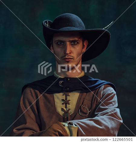 Portrait of brave man, medieval pirate in feathered hat staring intensely, against dark green vintage background. Portrait of brave man, medieval pirate in feathered hat staring intensely, against dark green vintage background. 122665501