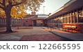 School courtyard with autumn leaves on a large tree, brick building, windows, and a bench bathed in soft, warm sunlight creating a tranquil atmosphere 122665595