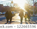 People crossing a street at sunrise with long shadows, urban surroundings, and a calm atmosphere, highlighting a morning commute or school drop-off 122665596