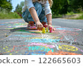 A child drawing with colorful chalk on the pavement, creating vibrant artwork outdoors on a sunny day, surrounded by nature 122665603