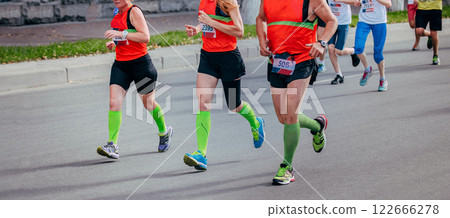 two women and man running marathon in city, green compression socks on his feet two women and man running marathon in city, green compression socks on his feet 122666278