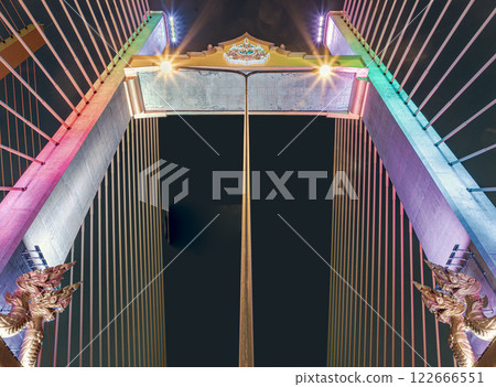 The girders of a cable-stayed bridge at Thotsamarachan Bridge or King Rama X Bridge with Two golden yellow Naga sculptures on concrete pillars at Night. 122666551