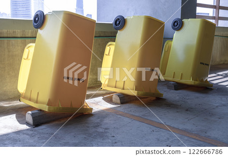 Perspective view of Yellow large plastic rubbish bins and turn upside down to dry near concrete wall on parking lot of condominium building. Perspective view of Yellow large plastic rubbish bins and turn upside down to dry near concrete wall on parking lot of condominium building. 122666786