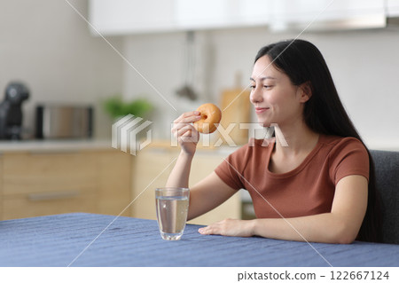 Asian woman looking at doughnut in the kitchen 122667124