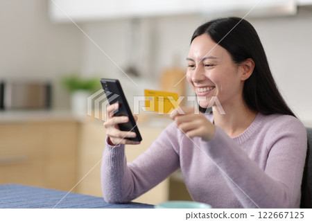 Happy asian woman buying online using card at home 122667125
