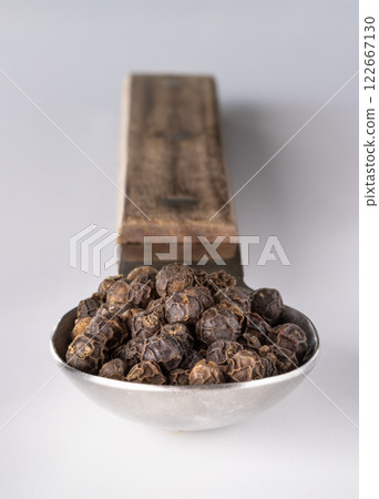 Perspective view of Raw organic black peppercorns or Dry black pepper seeds in stainless steel spoon isolated on the white background. Perspective view of Raw organic black peppercorns or Dry black pepper seeds in stainless steel spoon isolated on the white background. 122667130