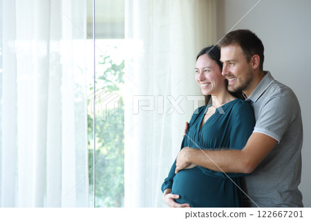 Asian pregnant woman and her husband looking through a window 122667201