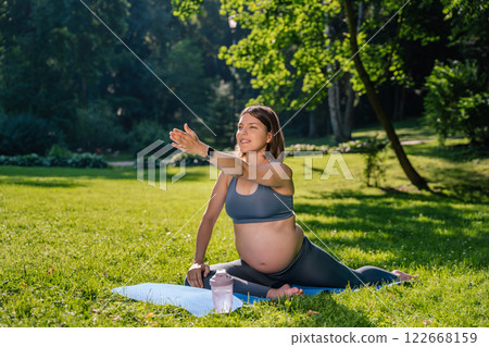 Pregnant young woman doing stretching exercises in the park in the morning 122668159