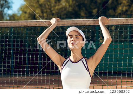 Young woman sitting on tennis court after workout resting from playing match 122668202