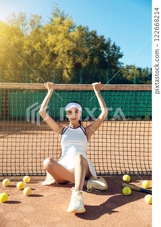Young woman sitting on tennis court after workout resting from playing match Young woman sitting on tennis court after workout resting from playing match 122668214