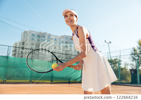 Slim woman playing tennis on court holding racket in motion enjoying outdoor summer workout 122668216