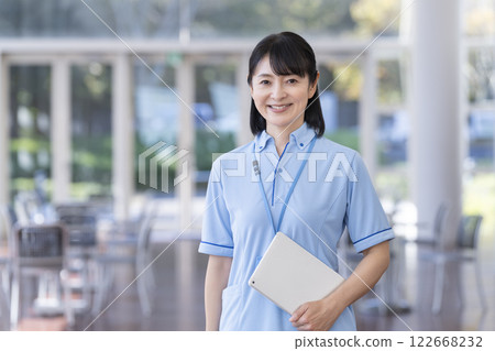 一名 50 多歲女性身穿藍色 Polo 衫，手拿平板電腦，看著鏡頭。 122668232