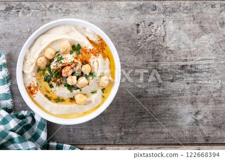 Chickpea hummus with olive oil, parsley and paprika in bowl on wooden table Chickpea hummus with olive oil, parsley and paprika in bowl on wooden table 122668394