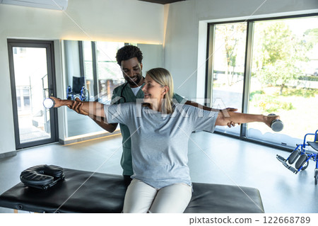 Male dark-skinned doctor working on arms stretching of his female patient 122668789