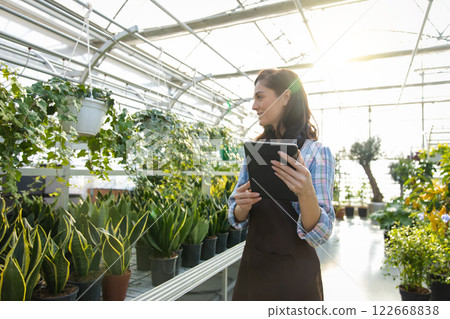 Female florist working in flower shop or botanical center growing plants and flowers in greenhouse 122668838