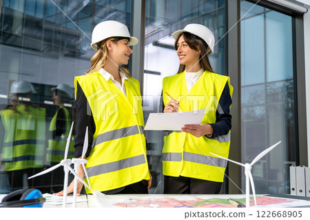 Two female engineers in yellow vest working together and looking excited Two female engineers in yellow vest working together and looking excited 122668905