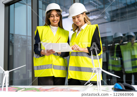 Two female engineers in yellow vest working together and looking excited Two female engineers in yellow vest working together and looking excited 122668906