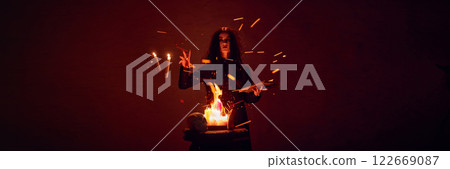 Terrifying woman with dark hair, with making spells with burning fire and spellbook against dark red background. Terrifying woman with dark hair, with making spells with burning fire and spellbook against dark red background. 122669087