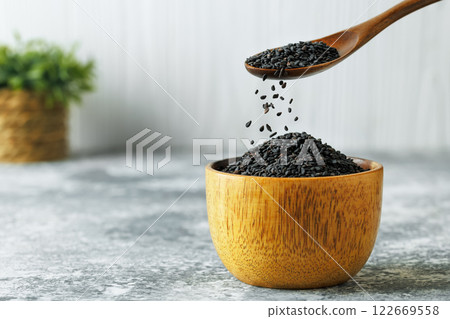 black sesame seeds falling from spoon in bowl on table 122669558