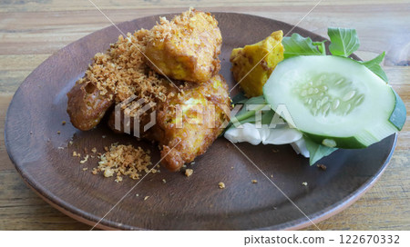 Savor Ayam Penyet, East Javanese fried chicken, pounded for tenderness, served with sambal, slice of cucumber, fried tofu, and tempeh. 122670332