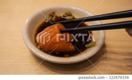 Hand is dipping salmon sushi into Shoyu sauce using chopsticks. 122670356