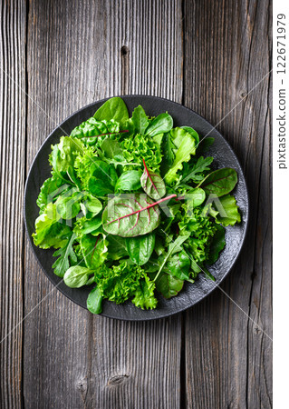 Mix of fresh juicy raw salad greens in black plate on wooden table 122671979