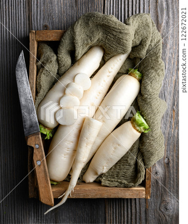 White daikon radish roots in wooden box with knife 122672021