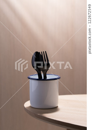 Black plastic spoon and fork in a white enamelware cup. Black plastic spoon and fork in a white enamelware cup. 122672549
