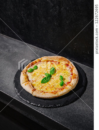 Freshly baked pizza with basil on a dark slate surface in a modern kitchen setting 122672695