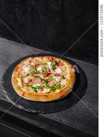 Delicious pizza topped with fresh ingredients on a dark stone surface in a modern kitchen setting 122672696